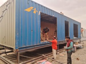 Close-up view of workers customizing a blue shipping container into a portable cabin.