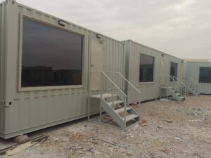 حاوية شحن معدنية رمادية مجهزة كمكتب موقع بأبواب ونوافذ وسلالم خارجية