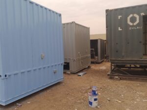 Modular prefab gray shipping container stored in a container modification workshop yard.