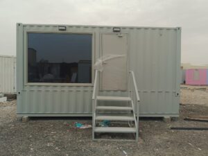 Front entrance of a prefab gray container office with tinted window and steel steps.