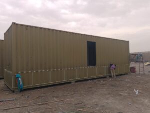 Long olive-green portable container undergoing window and door installation