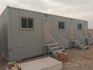 حاوية شحن معدنية رمادية مجهزة كمكتب موقع بأبواب ونوافذ وسلالم خارجية