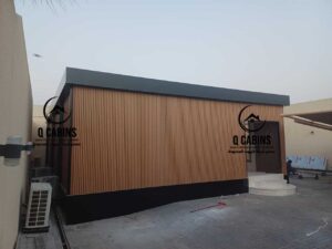 استراحة أو غرفة جاهزة مع إضاءة داخلية دافئة ونوافذ زجاجية واسعة تبرز جمال تشطيبات بديل الخشب