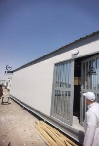 واجهة كابينة ساندوتش بانل بيضاء مزودة بنوافذ سحاب وحماية حديدية خارجية.
